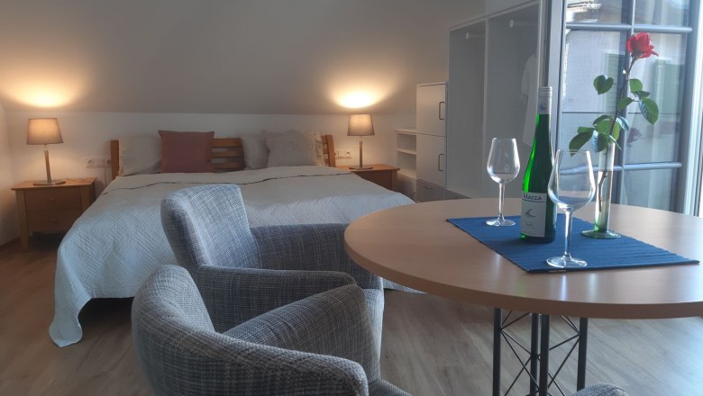 Cozy bedroom with double bed, table, two chairs, wine bottle and glasses.