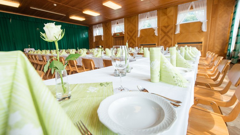 Festively decorated hall with long tables, green napkins and white roses.