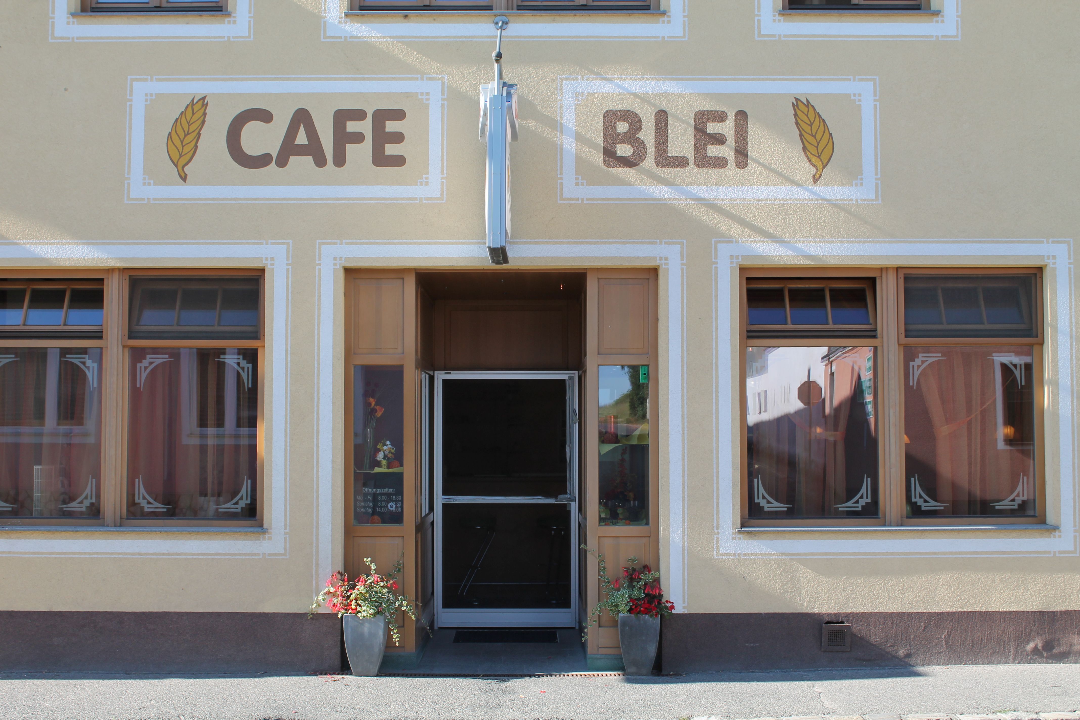 Entrance of a café with the inscription 'Cafe Blei' and floral decoration.