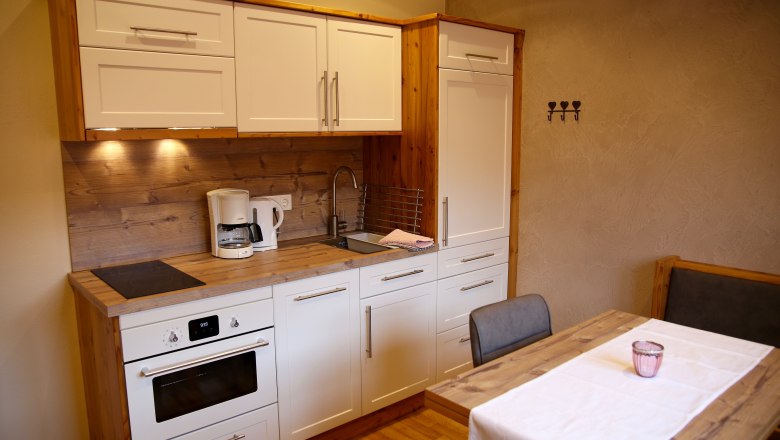 Modern kitchen with white cupboards, wooden worktop, dining table and chairs.