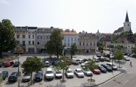 Town square in Hollabrunn with parked cars, historic buildings and a church in the background.