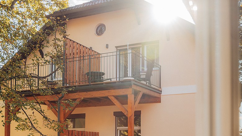 House with balcony and sunshine through trees.
