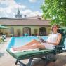 Woman in a white dress reads on a lounger by the pool.