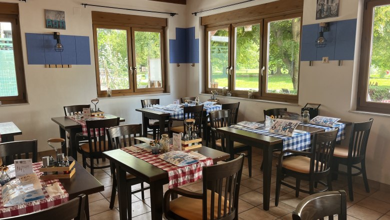Interior view of the pizzeria. Black furniture with red tablecloth and cutlery. The Aubad can be seen through the windows in the background,
