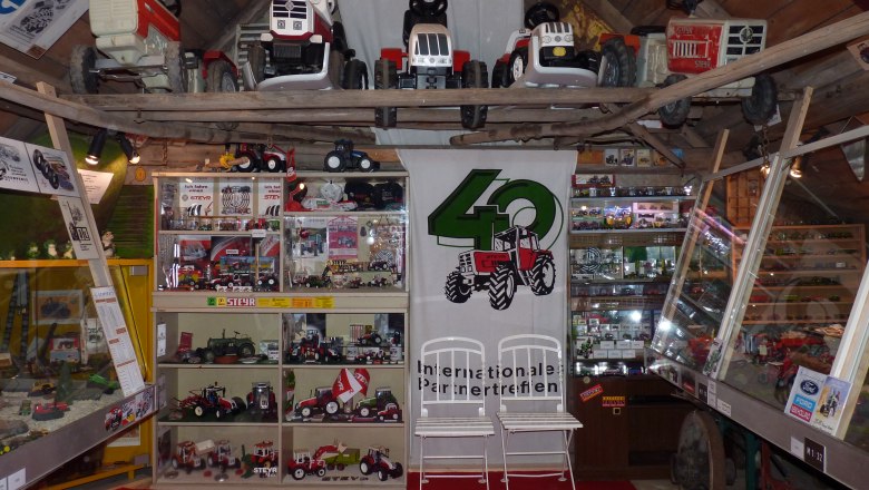 Exhibition of Steyr tractor models and toy tractors in a room with a wooden ceiling.