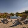 Two deckchairs on a wooden deck by the pond with garden in the background.