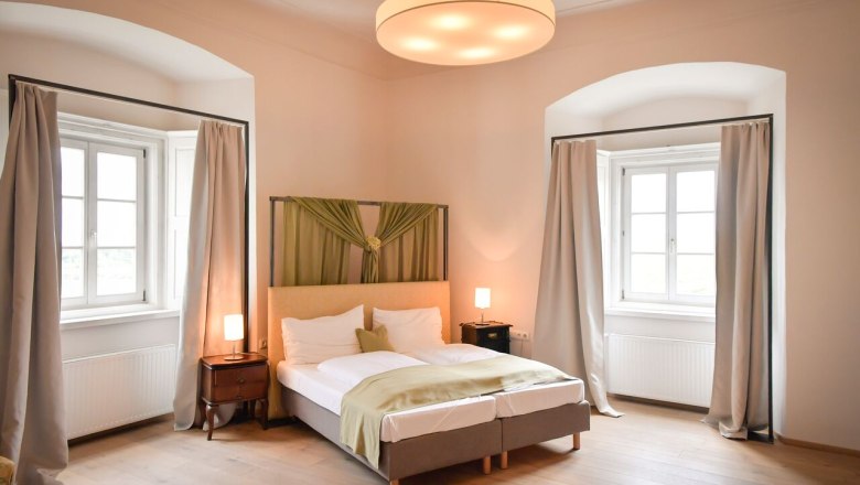 An elegant bedroom with a double bed, two windows with curtains and stylish lighting.