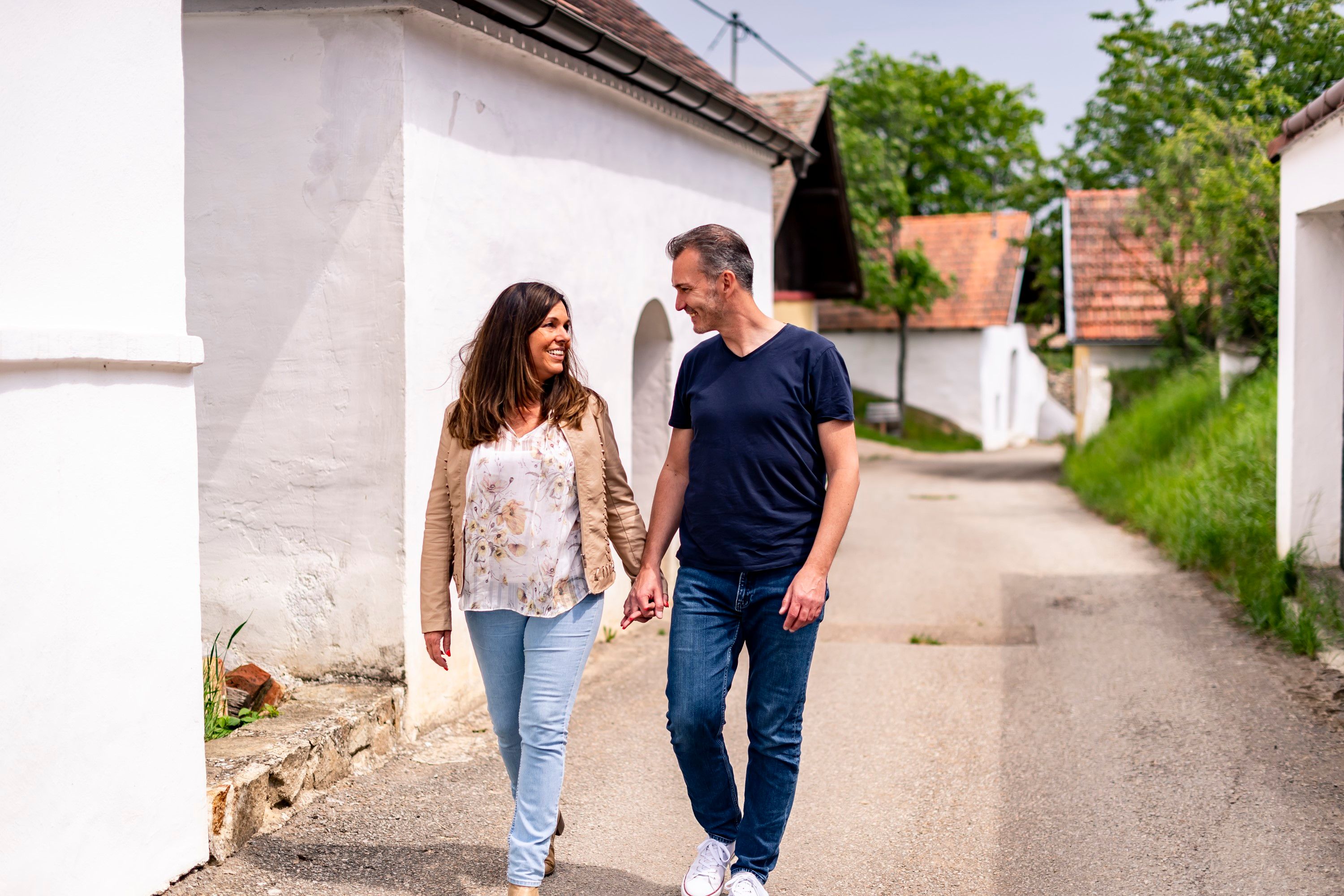 A couple walks hand in hand through the Öhlbergkellergasse in Pillersdorf, surrounded by traditional wine cellars and green countryside.