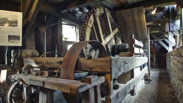 Interior view of a historic sawmill with large wooden cogwheels and wooden beams.