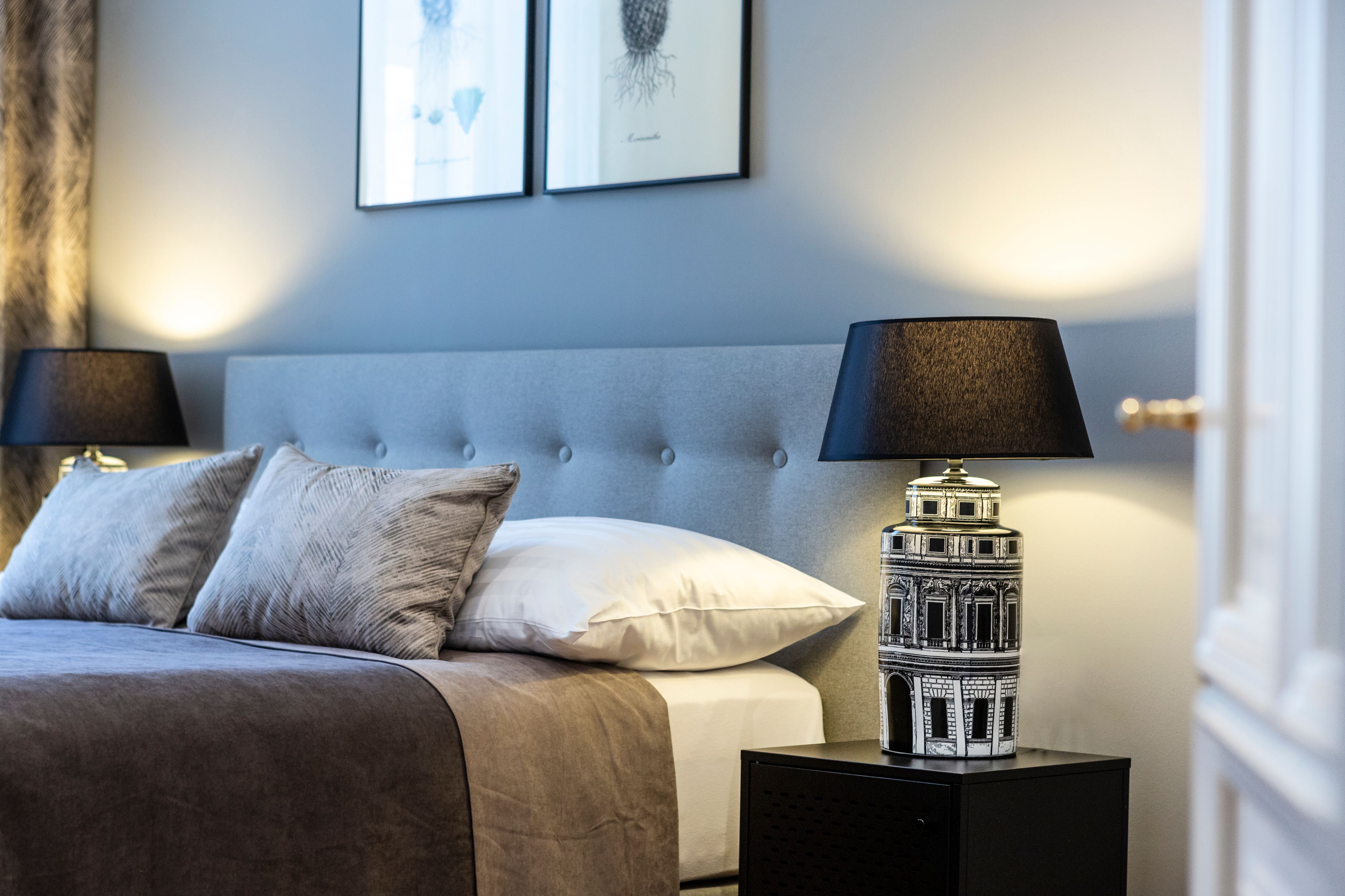 Elegant double room with gray headboard, two pillows, bedside lamp and wall pictures.
