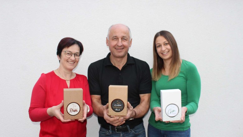 Three people hold gift boxes with rum, whiskey and gin in front of a white wall.