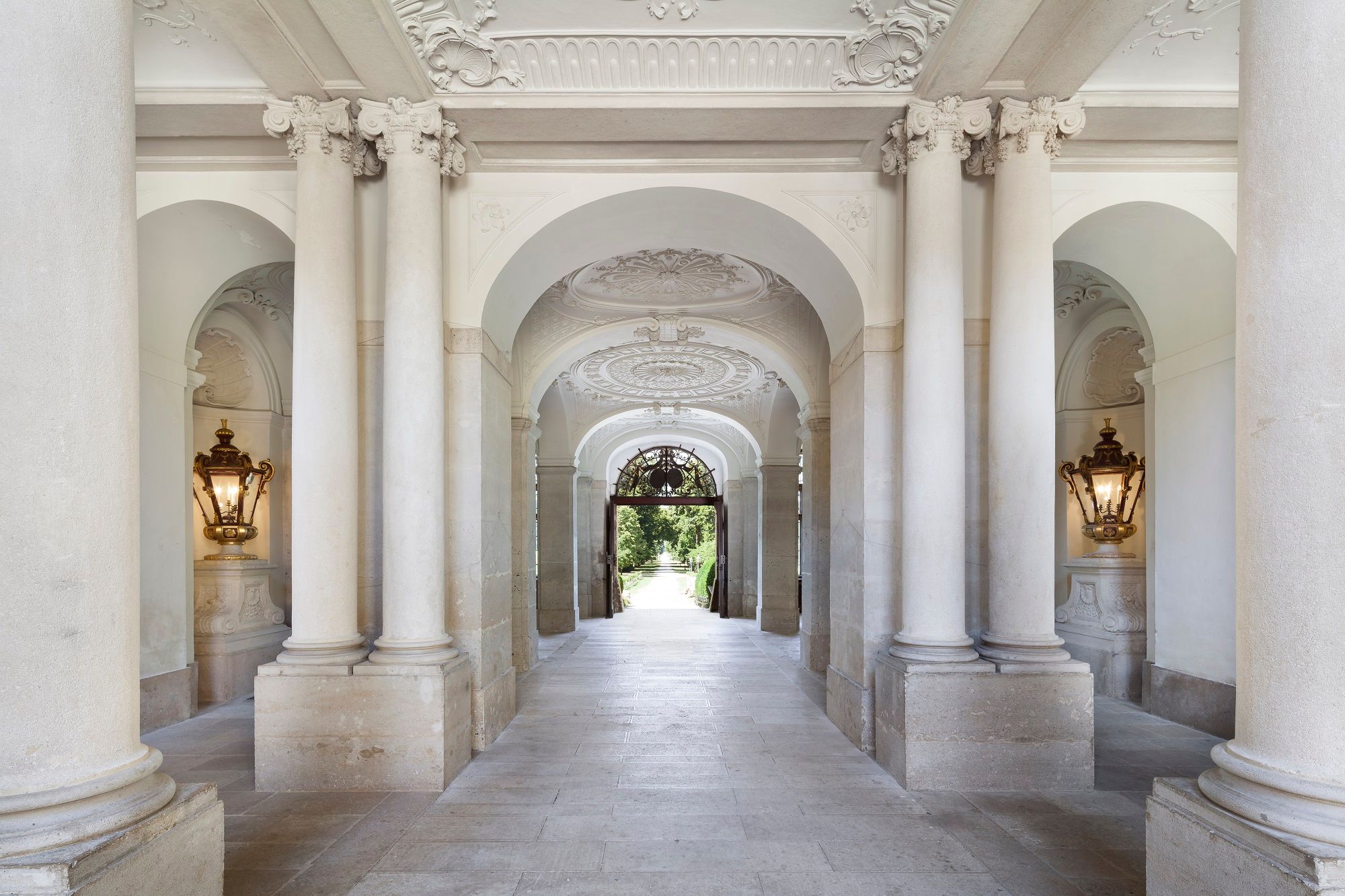 Elegant, column-lined passageway in Eckartsau Castle with ornate ceilings and wall lights.