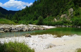 River landscape with clear water, pebble beach and wooded hills.