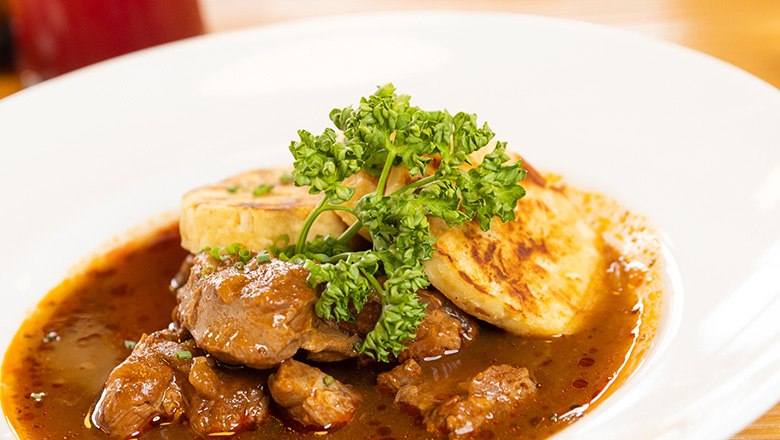 A plate of beef goulash and dumplings garnished with parsley.