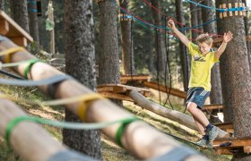A boy balances on a rope in a climbing park in the forest.