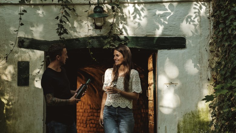 Two people are standing in front of a wine cellar on Schindergasse in Herrnbaumgarten.