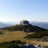 Mountain hut on a hill with a mountain panorama in the background.