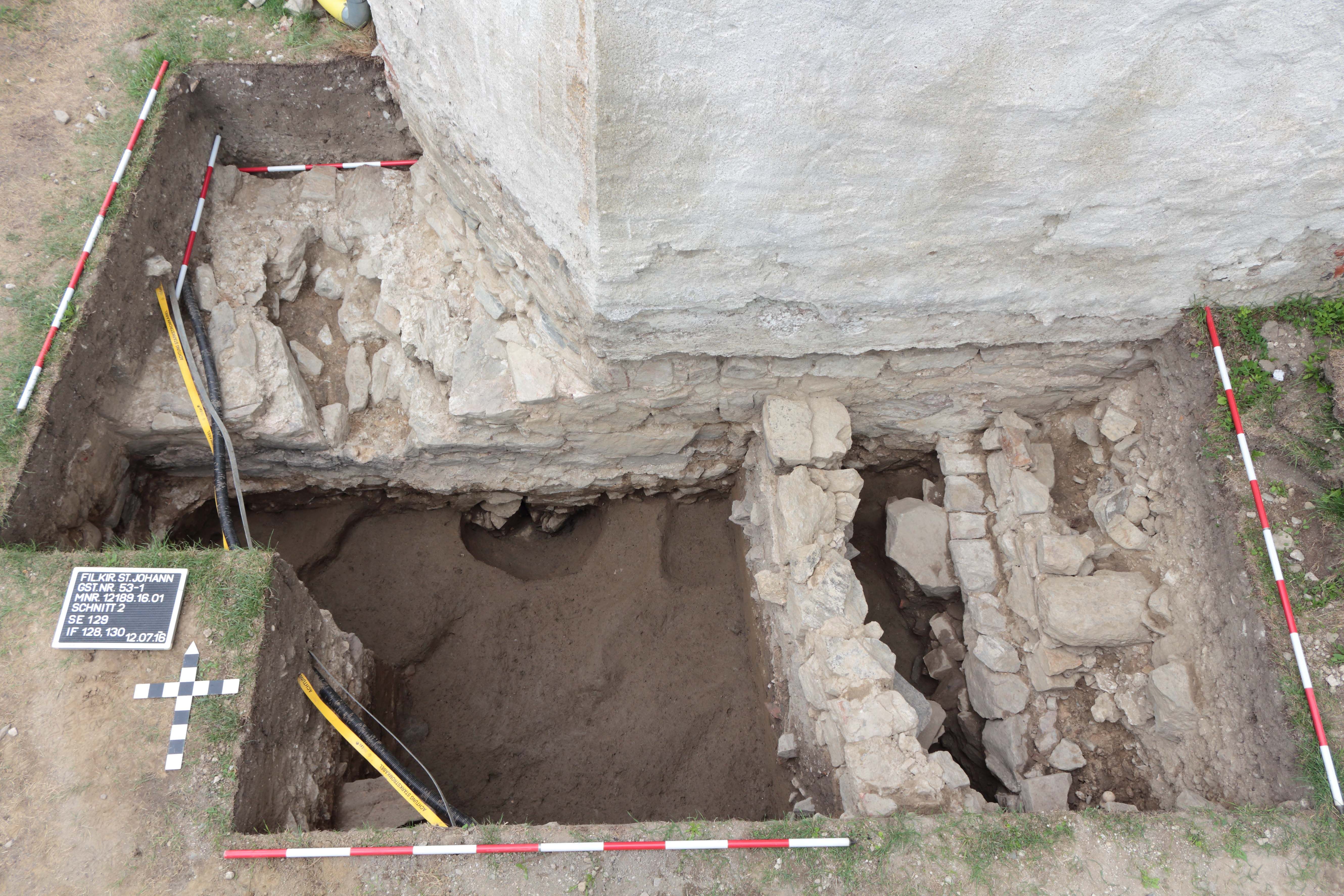 Archaeological excavation with uncovered wall remains and measuring sticks.