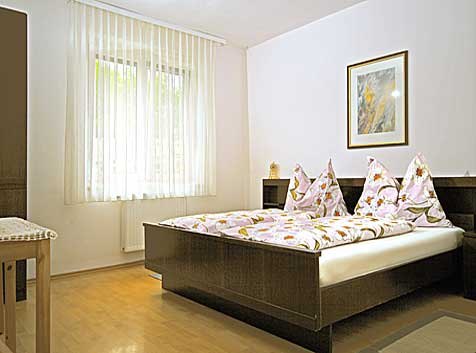A bright double room with a bed, a window with curtains and a picture on the wall.