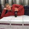 Person lying on wine cartons in the wine cellar, holding a wine bottle.