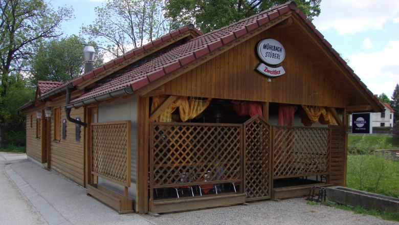 Wooden building with 'M&uuml;hlbachst&uuml;berl' sign and 'Zwettler' logo, surrounded by trees.