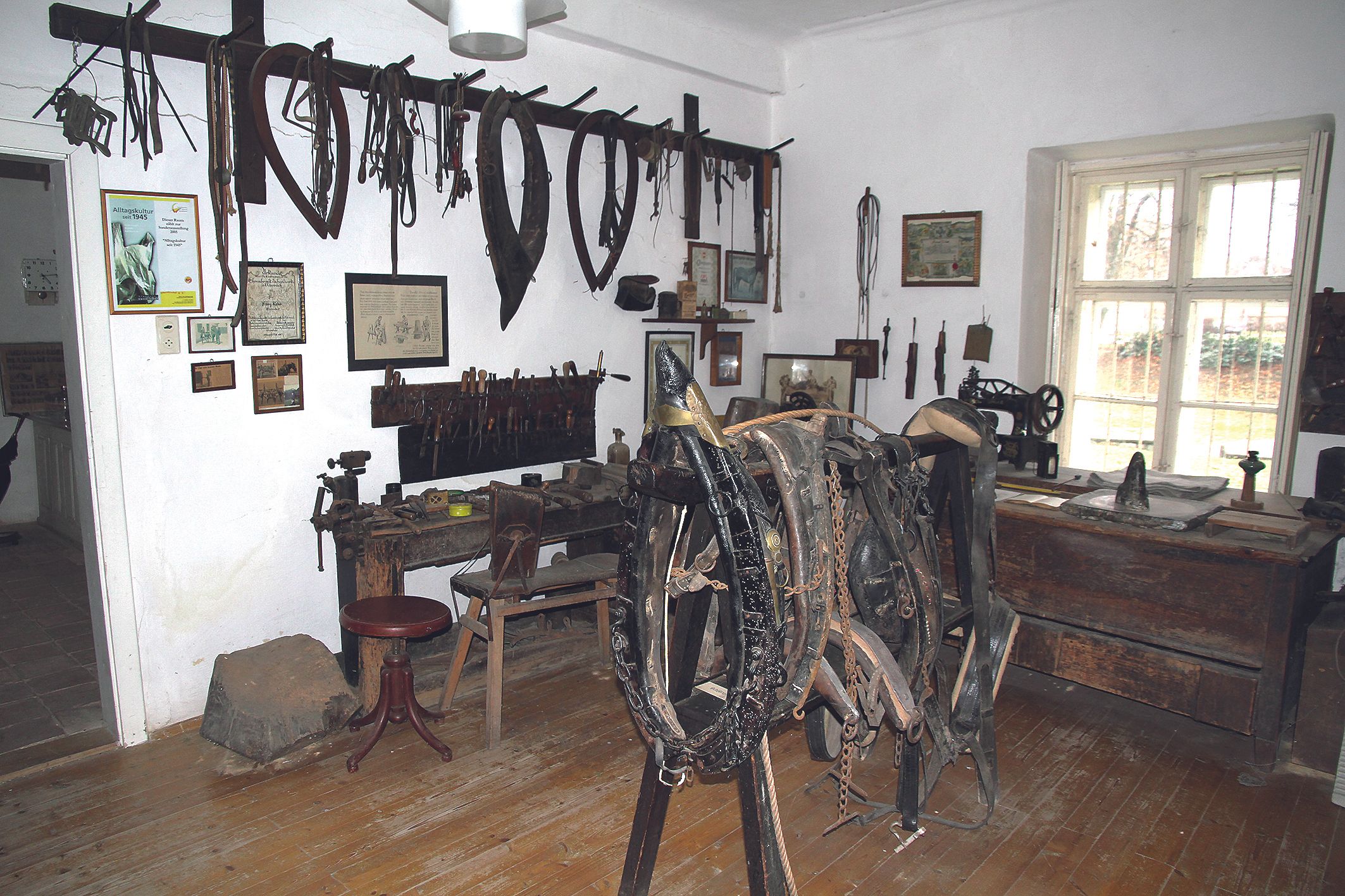 A room in a local history museum with old tools and horse harnesses on the walls.