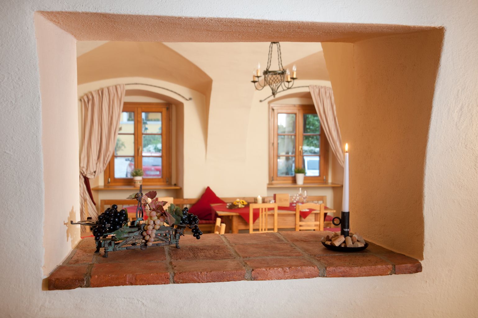 View through an opening in the wall into a cozy room with wooden furniture and candlelight.