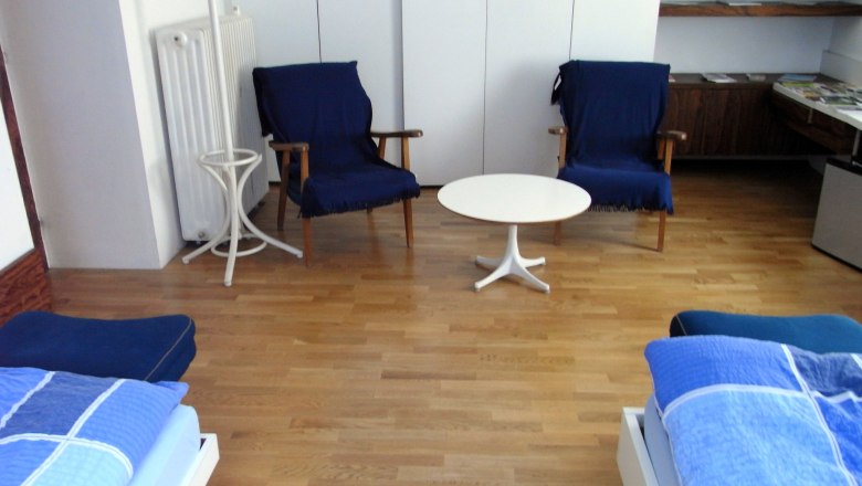 Linke Gert, Mag., © Mag. Linke A room with two blue armchairs, a white round table and two beds with blue bed linen on a wooden floor.