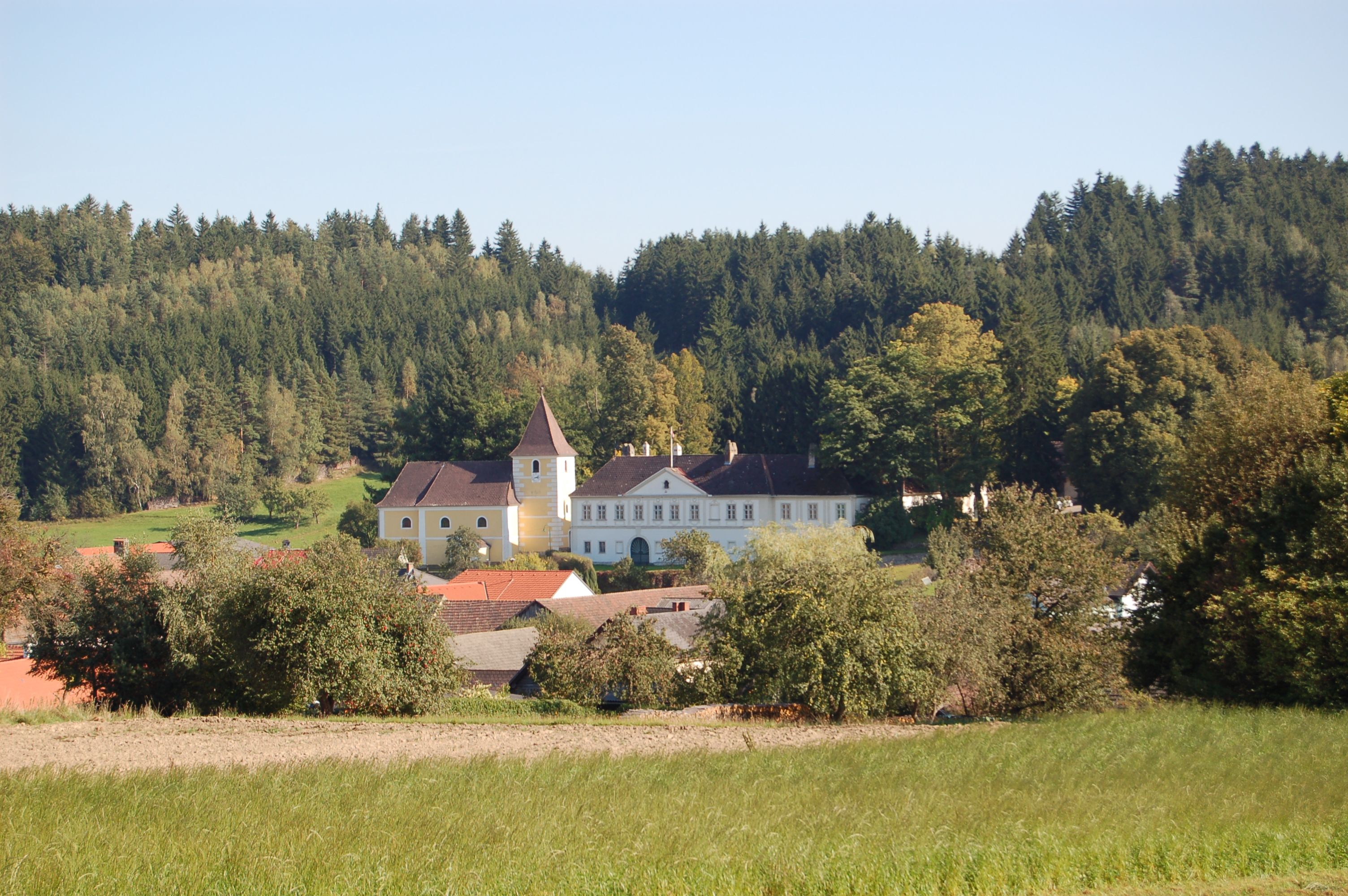 A castle with a yellow tower in the middle of a green landscape and surrounded by trees.