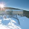 A snow-covered building with the inscription 'Ödenhof' in a wintry landscape, surrounded by trees and bright sunshine.