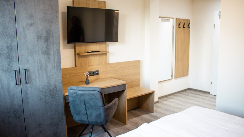 Modernly furnished hotel room with desk, TV, closet and mirror.