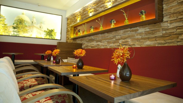 Interior view of a stylish day bar with wooden tables, red benches and decorative flower vases.