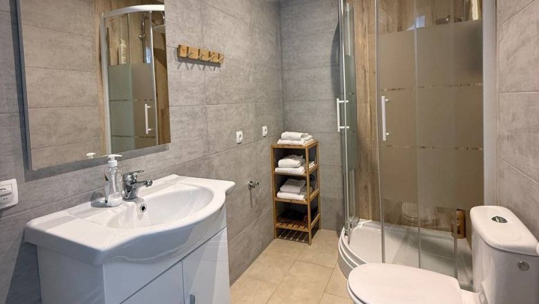 Modern bathroom with shower, washbasin and toilet. Towels are stacked on a shelf.