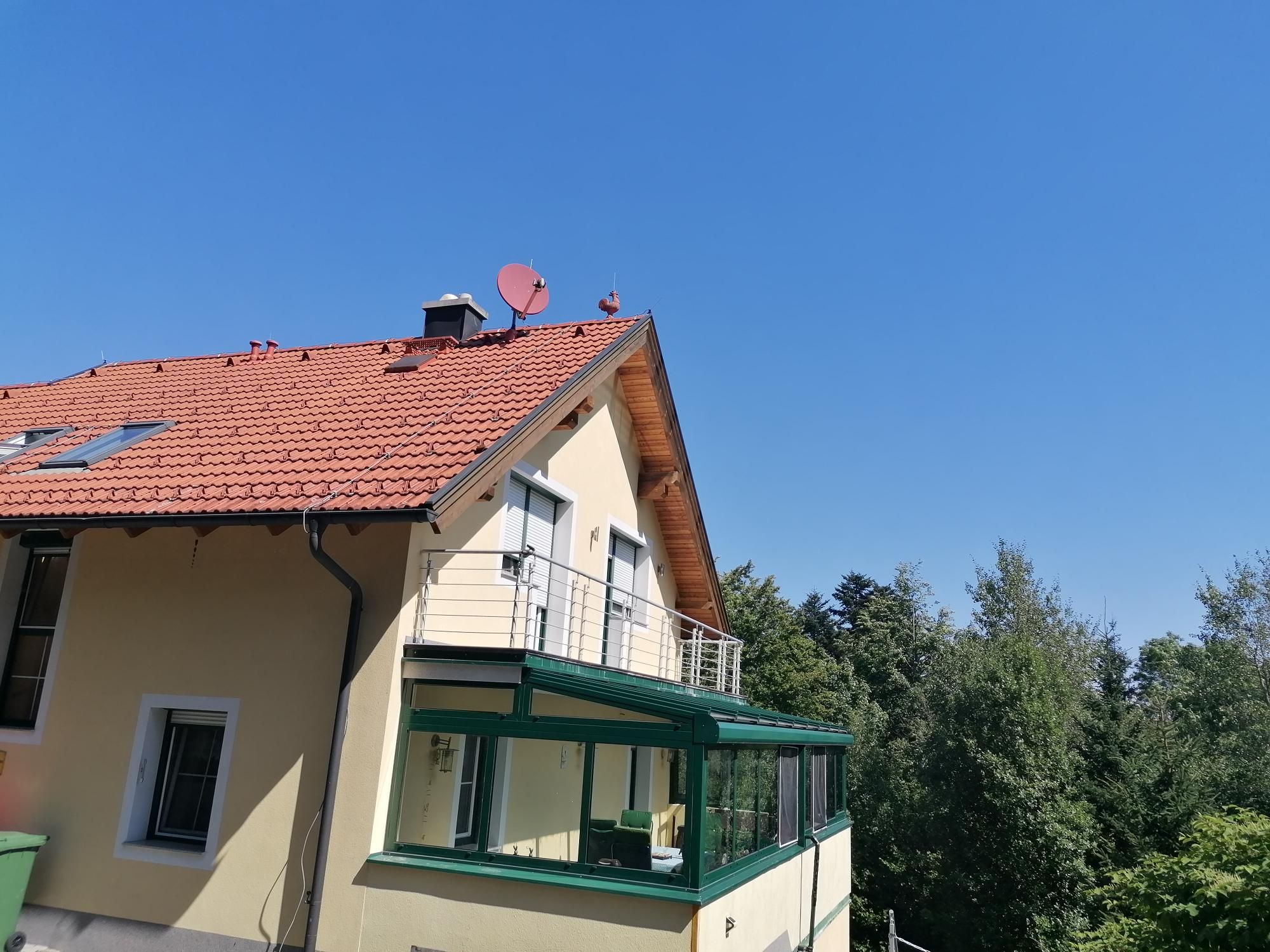 Yellow house with red roof and balcony, surrounded by trees, under a blue sky.