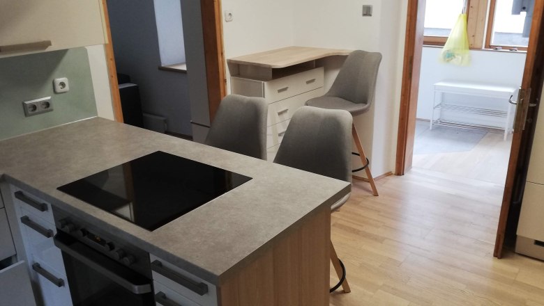 Modern kitchen with cooking island, two gray chairs and wooden floor.