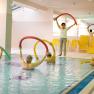 Senior citizens group doing water aerobics in the indoor pool with swimming noodles.