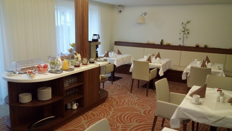 A breakfast room with laid tables and a buffet with food and drinks.