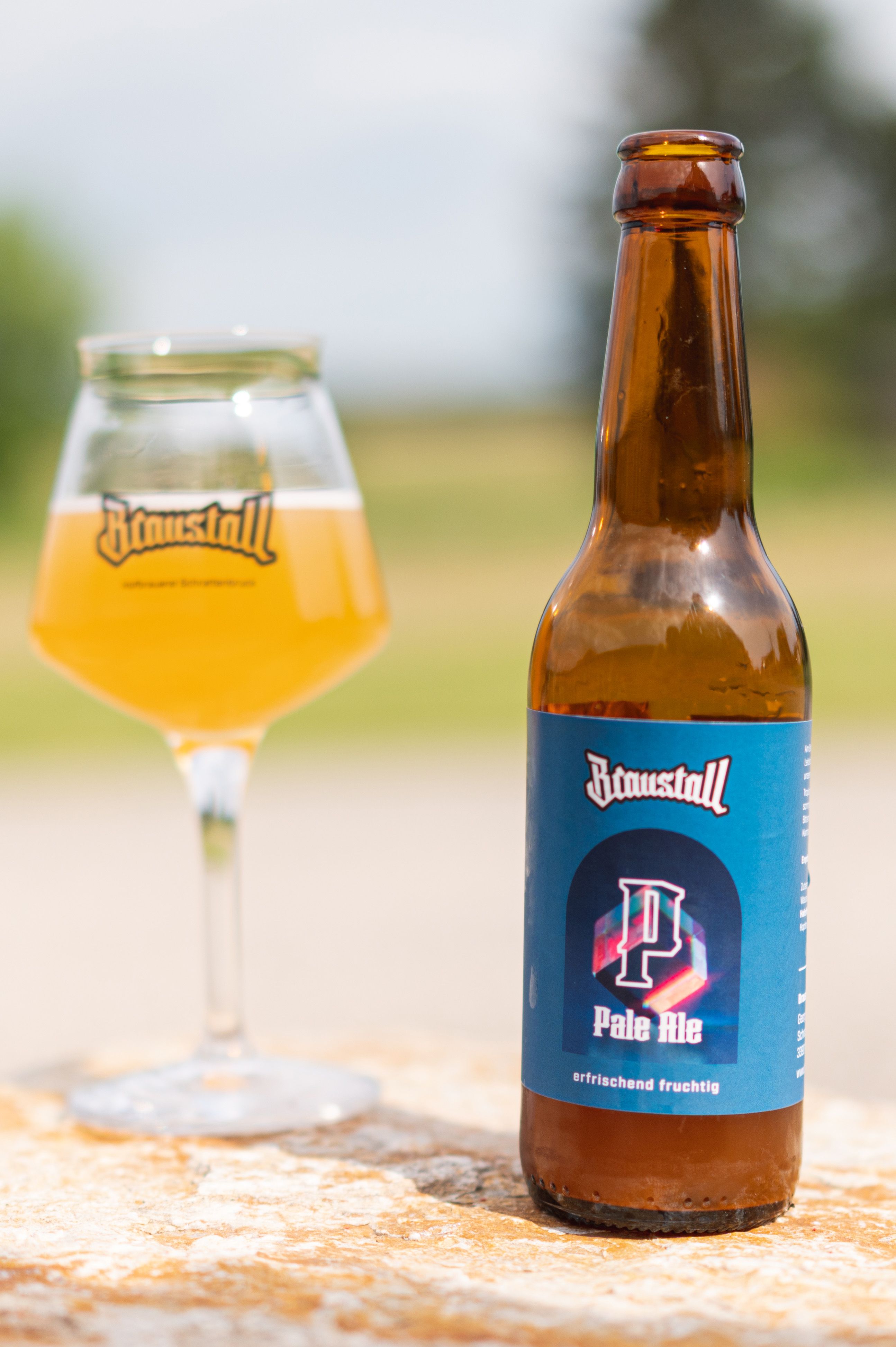 A bottle of Braustall Pale Ale and a glass of beer on a table outside.
