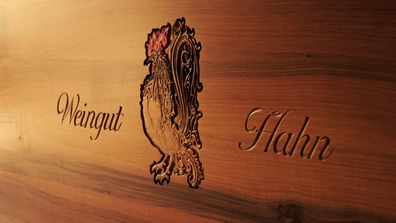 Wooden plaque with engraved rooster and 'Weingut Hahn' lettering.