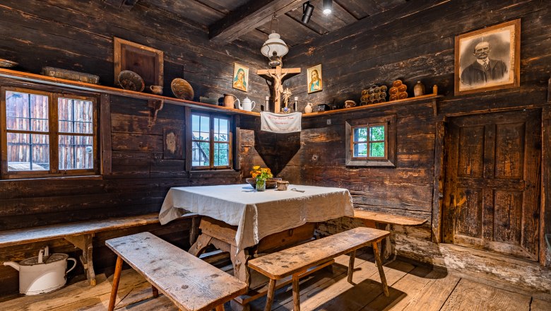 Rustic room with wooden walls, table with white cloth, benches, religious pictures and antique objects.