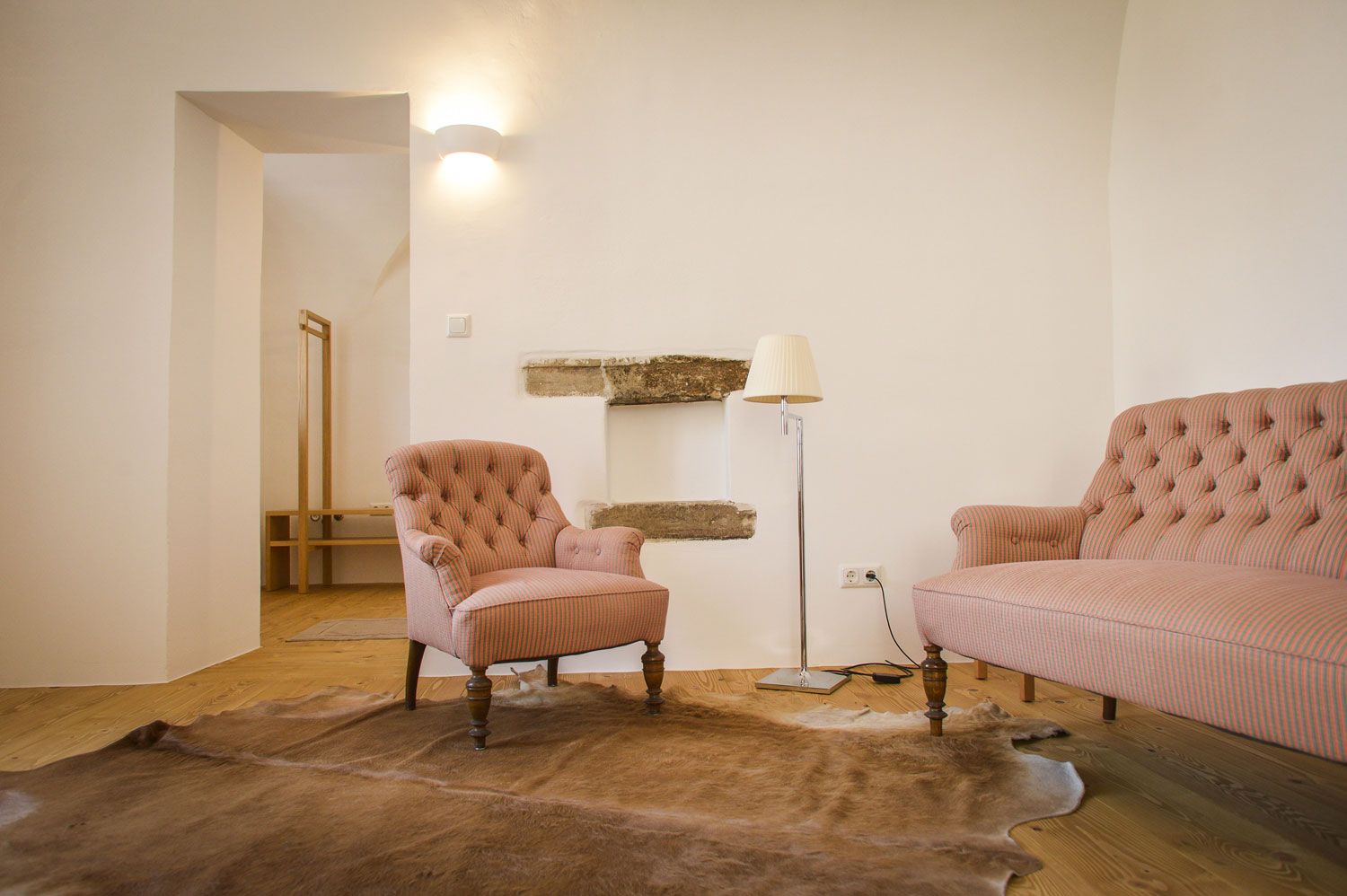 A cozy room with a pink striped armchair and sofa, a floor lamp and a fur rug on a wooden floor.