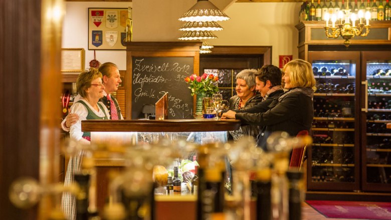 People in a cozy restaurant with bottles of wine in the background.