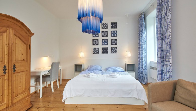 Bedroom with double bed, blue and white curtains, wooden floor and a large wooden wardrobe.
