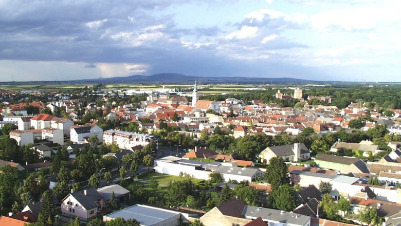 Aerial view of Bruck an der Leitha with houses and church, surrounded by green landscape and cloudy sky.