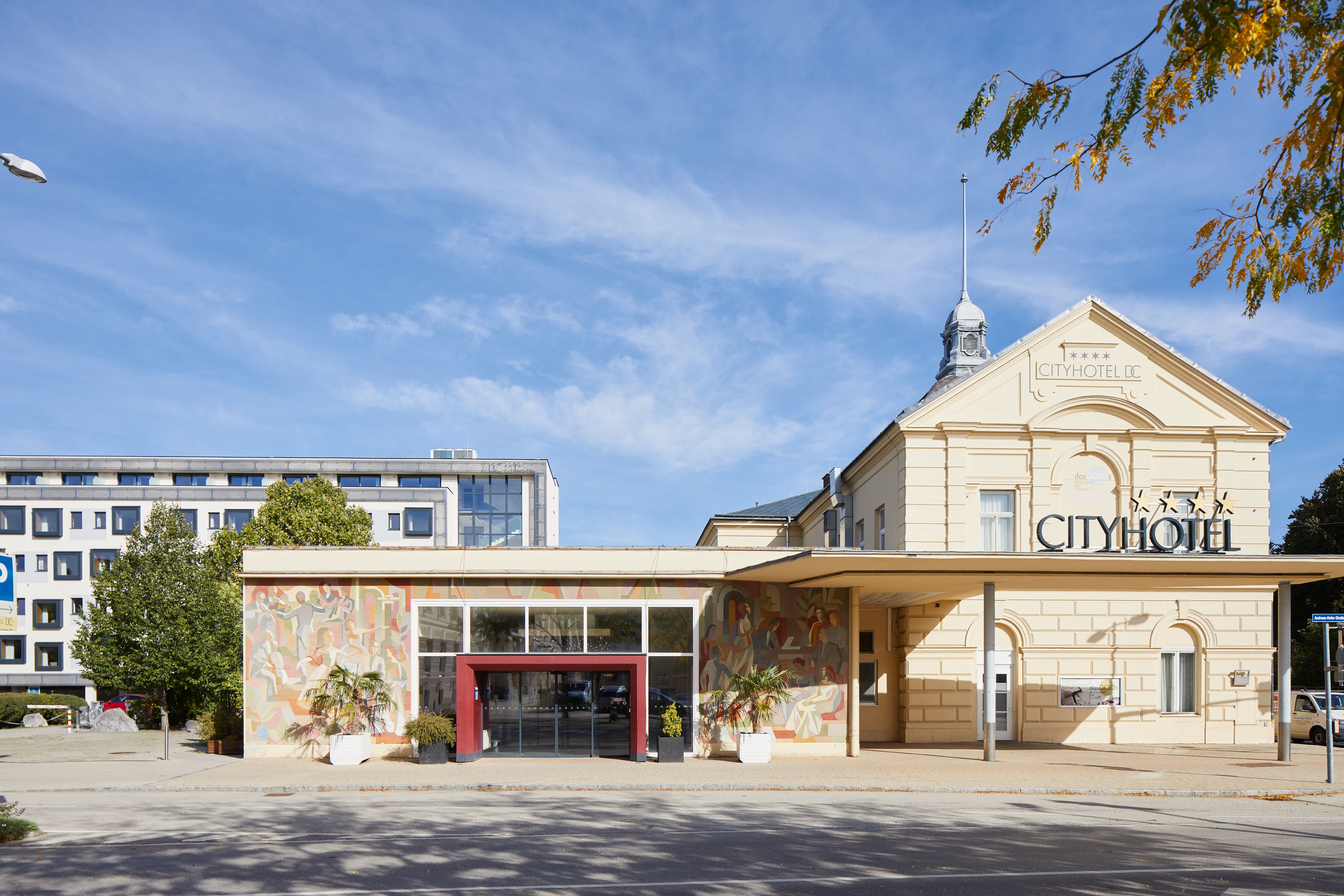 Modern hotel building with glass balconies and trees in the foreground.