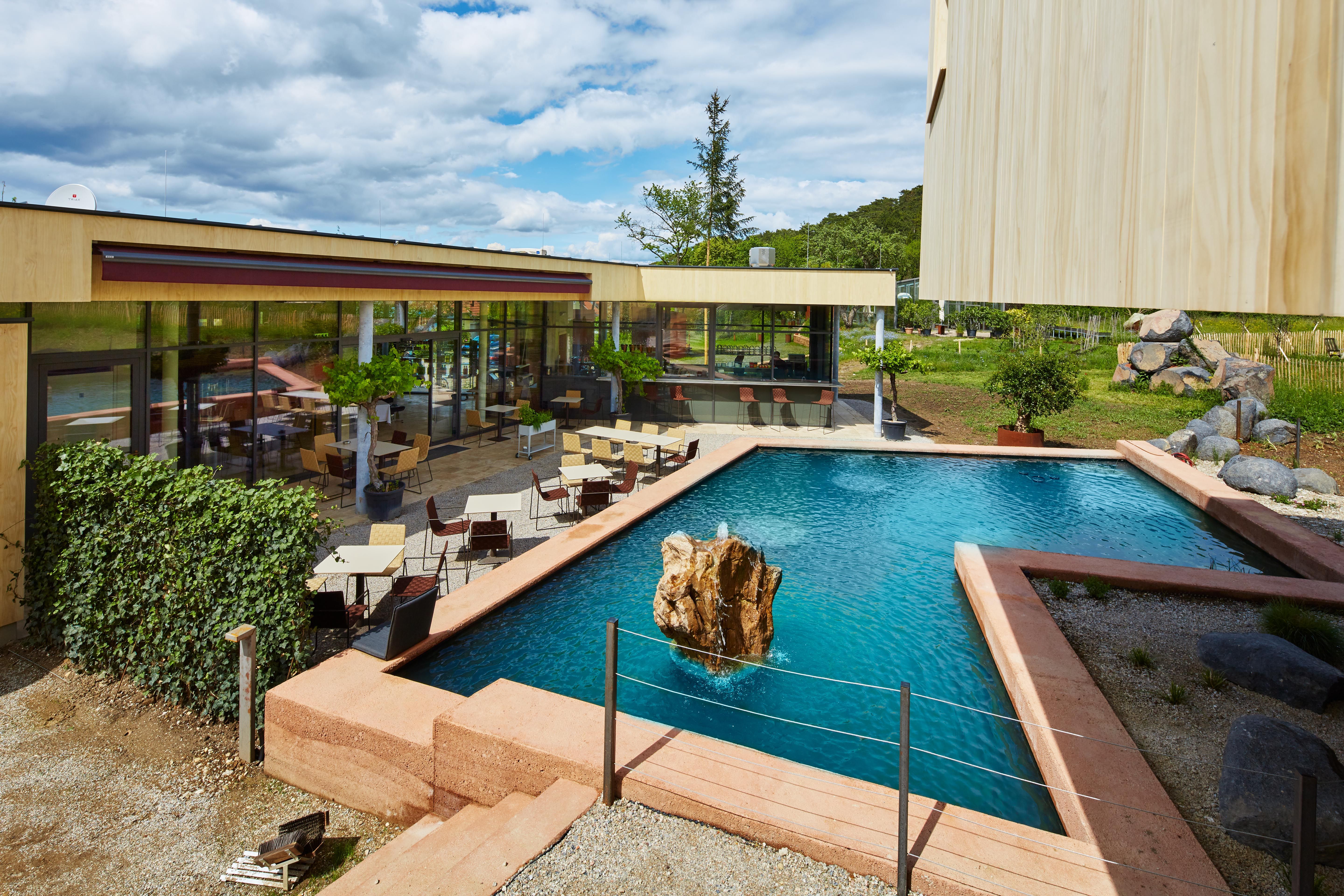 Modern terrace with tables and chairs next to a rectangular pond with rocks in the middle.