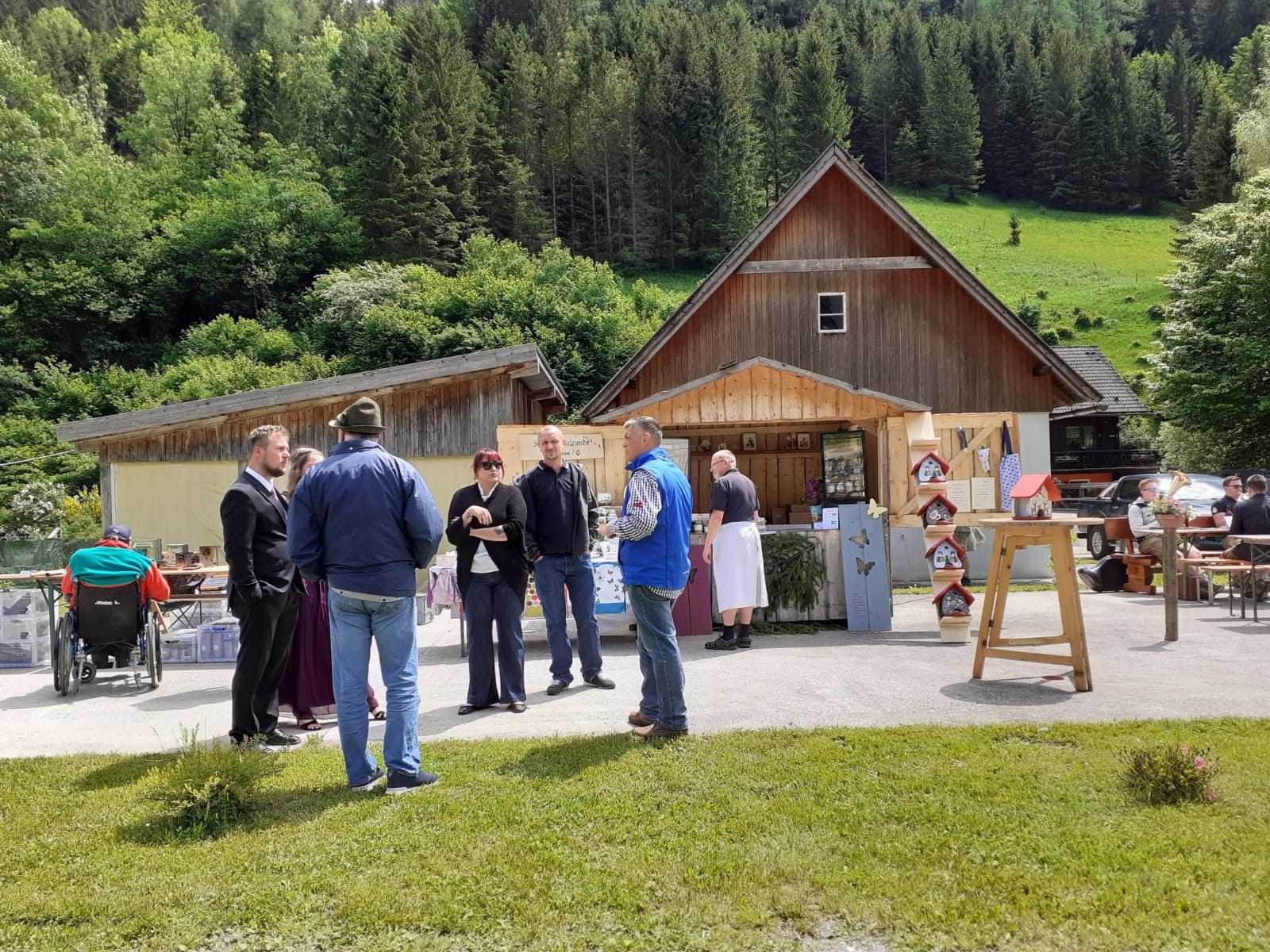 People at a market in front of wooden huts in a rural setting.