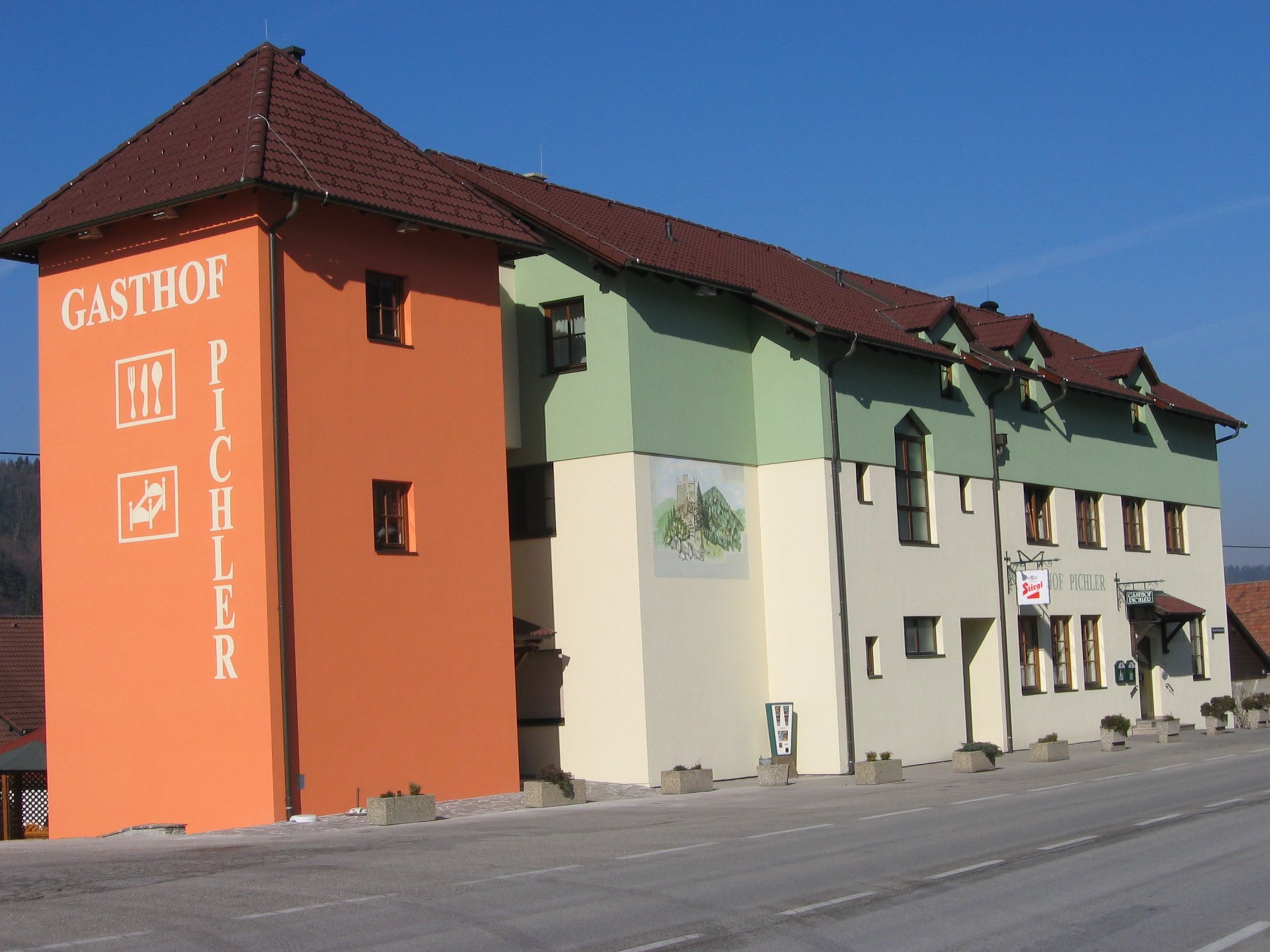 An inn with an orange tower and green and white façade on a street.