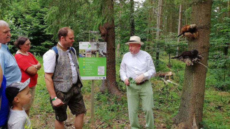 Group of people in the forest listening to a man standing in front of a sign in Geras Nature Park.