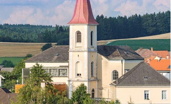 Hochwolkersdorf parish church with red, pointed tower roof and surrounding landscape.
